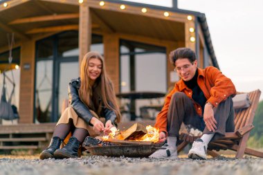 Genç sevgili sevgili sevgili, şöminenin yanında, kırsal kesimdeki ahşap bir kulübede oturmuş, şekerleme kızartıyorlar.