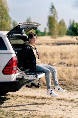 Adamın biri, ormanda ve bozkırda güzel yerlerde seyahat ederken bir arabanın bagajında oturuyor.