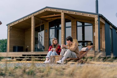 Terasta, büyük bir evin yanında birbirine aşık bir çift, tahta koltuklarda çay içip birbirleriyle iletişim kurarlar.