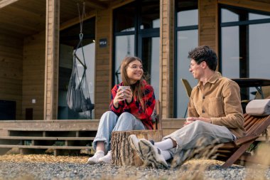 Terasta, büyük bir evin yanında birbirine aşık bir çift, tahta koltuklarda çay içip birbirleriyle iletişim kurarlar.