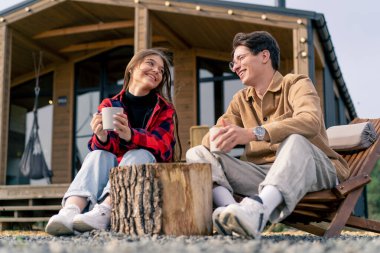 Terasta, büyük bir evin yanında birbirine aşık bir çift, tahta koltuklarda çay içip birbirleriyle iletişim kurarlar.