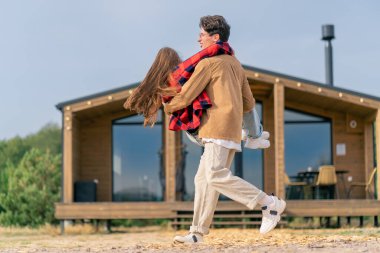 Genç bir adam, sevgili kızını şehir dışındaki evinin önünde kollarında döndürüyor.