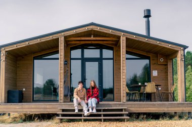 Birbirine aşık genç bir çift büyük ahşap bir kulübenin merdivenlerinde birlikte oturuyor.