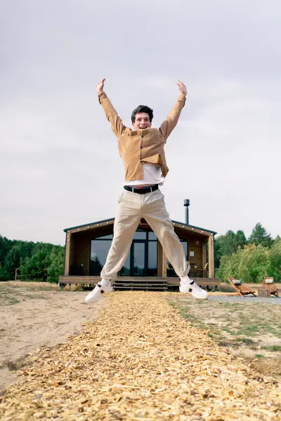 一个快乐的小伙子在林地里的一座大木屋前欢快地跳着 — 图库照片