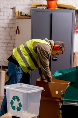 Ses geçirmez kulaklık takan bir atık geri dönüşüm istasyonu çalışanı kullanılmış plastik kapakları parçalamak için özel bir makineyi çalıştırıyor.