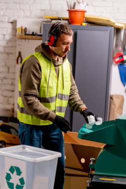 Ses geçirmez kulaklık takan bir atık geri dönüşüm istasyonu çalışanı kullanılmış plastik kapakları parçalamak için özel bir makineyi çalıştırıyor.