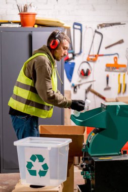 Ses geçirmez kulaklık takan bir atık geri dönüşüm istasyonu çalışanı kullanılmış plastik kapakları parçalamak için özel bir makineyi çalıştırıyor.