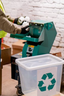 Erkek eli eldivenli yakın çekim. Plastik kapakları geri dönüşüm için öğütme aparatına döküyor.