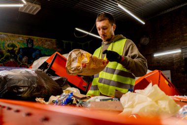 Üniformalı ve eldivenli bir çalışan atık geri dönüşüm istasyonunda çöpleri ayırıyor ve sınıflandırıyor.