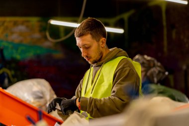 Üniformalı bir adamın çöp dağıtım hattı üzerinde çalışmasını ve atığı özel konteynırlara ayırmasını.