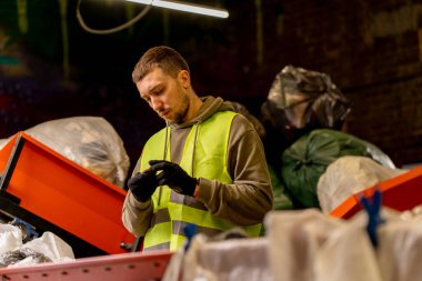 Atık öğütme istasyonunda çalışırken çöpleri özel bir sıralama hattında sıralayan eldivenli bir koruyucu yelek.