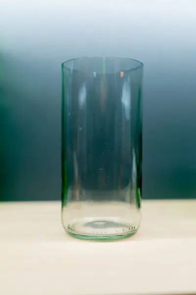 A glass tumbler made of colored transparent glass stands on a wooden table in a handmade decor store