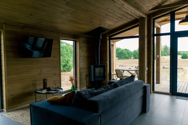 Large spacious living room with panoramic windows overlooking the forest with a soft sofa and TV in wooden house