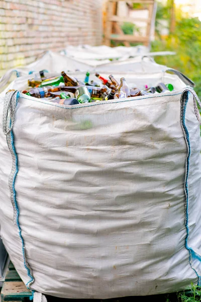 A large heavy bag with a huge amount of used glass bottles is prepared for their disposal at a waste recycling station
