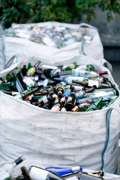 大量の使用済みガラスボトルを備えた大型重いバッグは 廃棄物リサイクルステーションで処分するために用意されています — ストック写真