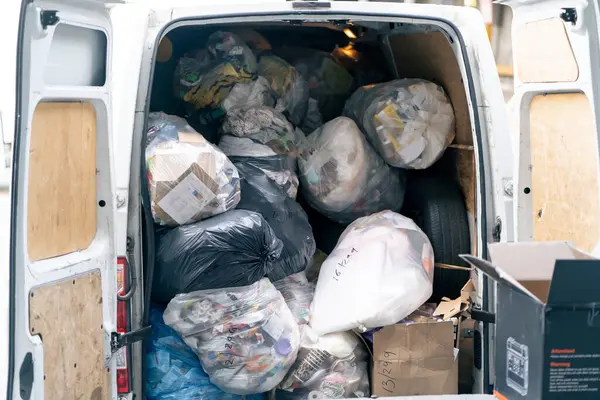 A garbage truck is fully loaded with large black bags of garbage and waste of various origins