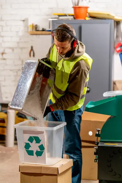 A waste recycling plant employee in uniform and headphones pours shredded plastic caps into a container for recycling