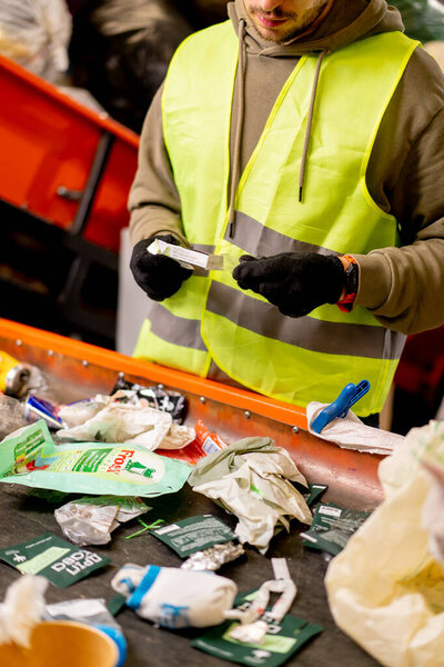 Hands in gloves of a uniformed employee sort garbage into categories on a special line at a waste recycling plant