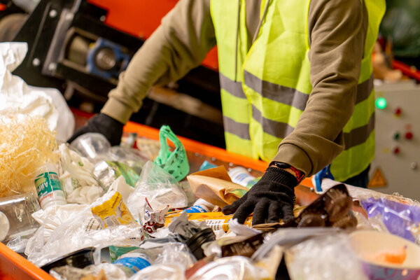 Hands in gloves of a uniformed employee sort garbage into categories on a special line at a waste recycling plant