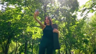 Eğitimden önce ya da sonra parkta yürüyüş yapan aktif, güzel bir yogi kadın telefonda fotoğraf çekerken elinde spor paspası tutuyor.