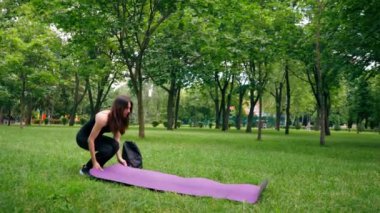 Kız yoga meditasyonuna başlamak için parkta çimlerin üzerine bir spor minderi seriyor.
