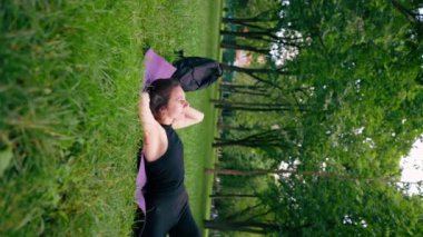 Dikey video aktif güzel yogi kadın antrenmandan sonra şehir parkında dinleniyor spor minderinin üzerinde gökyüzüne bakıyor.