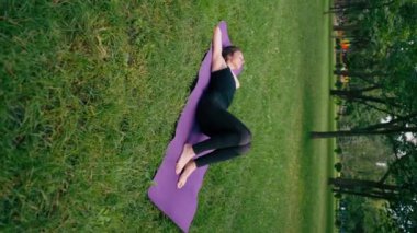 Dikey video aktif güzel yogi kadın antrenmandan sonra şehir parkında dinleniyor spor minderinin üzerinde gökyüzüne bakıyor.