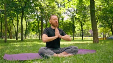 Yakışıklı sakallı adam parkta meditasyon yapıyor. Lotus pozisyonunda oturuyor. Yoga yapıyor.