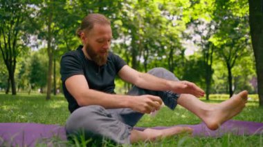 Yakışıklı sakallı adam parkta meditasyon yapıyor. Lotus pozisyonunda oturuyor. Yoga yapıyor.