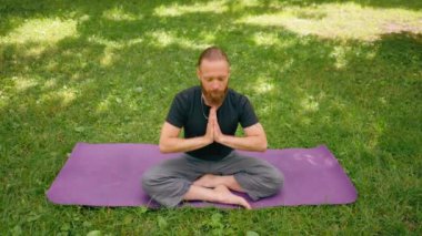 Yakışıklı sakallı adam parkta meditasyon yapıyor. Lotus pozisyonunda oturuyor. Yoga yapıyor.