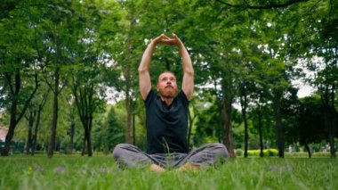 Yakışıklı sakallı adam parkta meditasyon yapıyor yoga yapıyor esneme hareketleri yapıyor ve farklı kas grupları çalıştırıyor.
