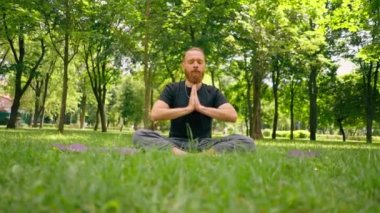 Yakışıklı sakallı adam parkta meditasyon yapıyor. Lotus pozisyonunda oturuyor. Yoga yapıyor.