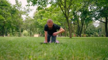 Yakışıklı sakallı adam parkta meditasyon yapıyor yoga yapıyor esneme hareketleri yapıyor ve farklı kas grupları çalıştırıyor.