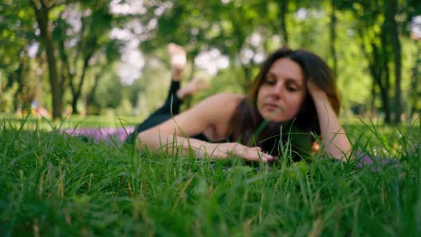 クローズアップアクティブな美しいヨギ女性は 空を見ているフィットネスマットに横たわった後 市内公園に休んでいます — ストック動画