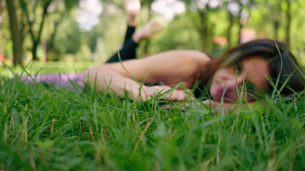 クローズアップアクティブな美しいヨギ女性は 空を見ているフィットネスマットに横たわった後 市内公園に休んでいます — ストック動画