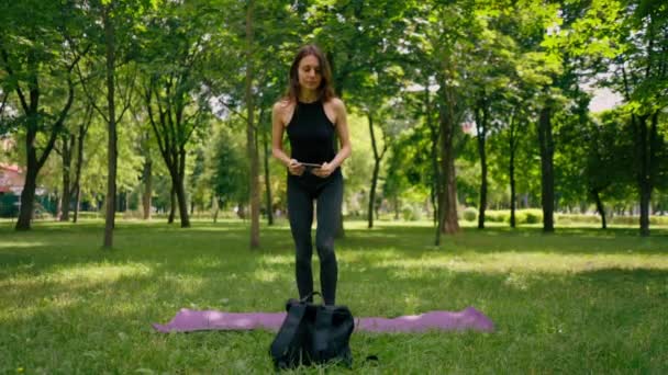소녀는 명상을 연습을 시작하기 공원에서 잔디에 피트니스 매트를 가방에서 장비를 — 비디오