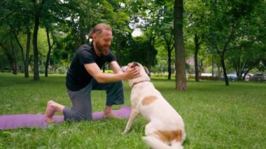 Şehir parkında yoga ve meditasyon yaparken gülümseyen bir adam sokak köpeğini okşuyor.