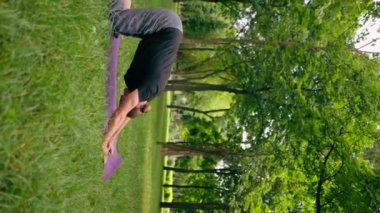 Dikey video yakışıklı sakallı adam parkta meditasyon yapıyor yoga yapıyor esneme hareketleri yapıyor ve farklı kas grupları çalıştırıyor.