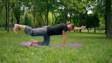 Yakışıklı sakallı adam parkta meditasyon yapıyor yoga yapıyor esneme hareketleri yapıyor ve farklı kas grupları çalıştırıyor.