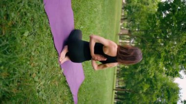 dikey video görüntüsü deneyimli bir bayan eğitmen parkta meditasyon yapar yoga yapar ve farklı kas grupları çalıştırır.