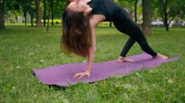 Deneyimli bir kadın eğitmen parkta meditasyon yapar yoga yapar ve farklı kas grupları çalıştırır.