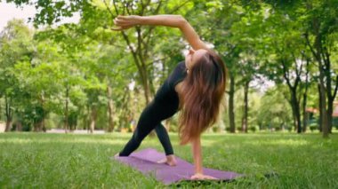 Deneyimli bir kadın eğitmen parkta meditasyon yapar yoga yapar ve farklı kas grupları çalıştırır.