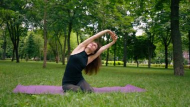 Deneyimli bir kadın eğitmen parkta meditasyon yapar yoga yapar ve farklı kas grupları çalıştırır.