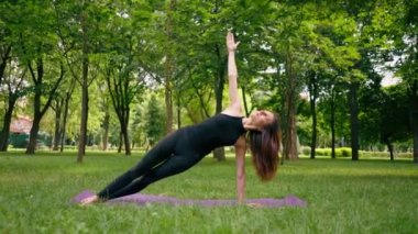 Deneyimli bir kadın eğitmen parkta meditasyon yapar yoga yapar ve farklı kas grupları çalıştırır.