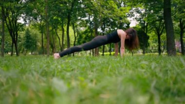 Deneyimli bir kadın eğitmen parkta meditasyon yapar yoga yapar ve farklı kas grupları çalıştırır.