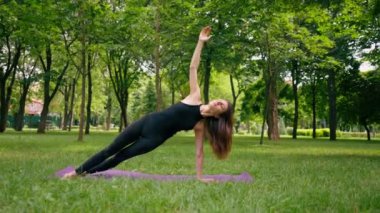 Deneyimli bir kadın eğitmen parkta meditasyon yapar yoga yapar ve farklı kas grupları çalıştırır.