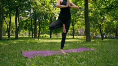 Tecrübeli bir kadın eğitmen parkta meditasyon yapıyor yoga yapıyor tek bacağı esnetiyor ve farklı kas grupları çalıştırıyor.
