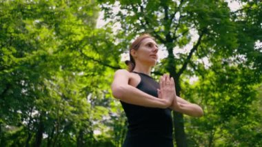 Deneyimli bir kadın eğitmen parkta meditasyon yapar yoga yapar ve farklı kas grupları çalıştırır.