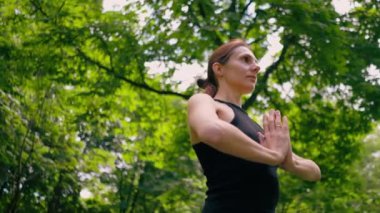 Deneyimli bir kadın eğitmen parkta meditasyon yapar yoga yapar ve farklı kas grupları çalıştırır.
