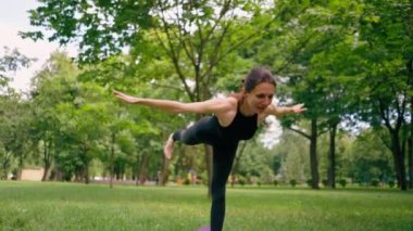 Tecrübeli bir kadın eğitmen parkta meditasyon yapıyor yoga yapıyor tek bacağı esnetiyor ve farklı kas grupları çalıştırıyor.
